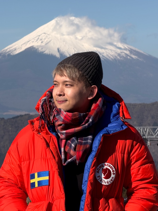 Izac in a red winter jacket with a snow-covered mountain behind him.